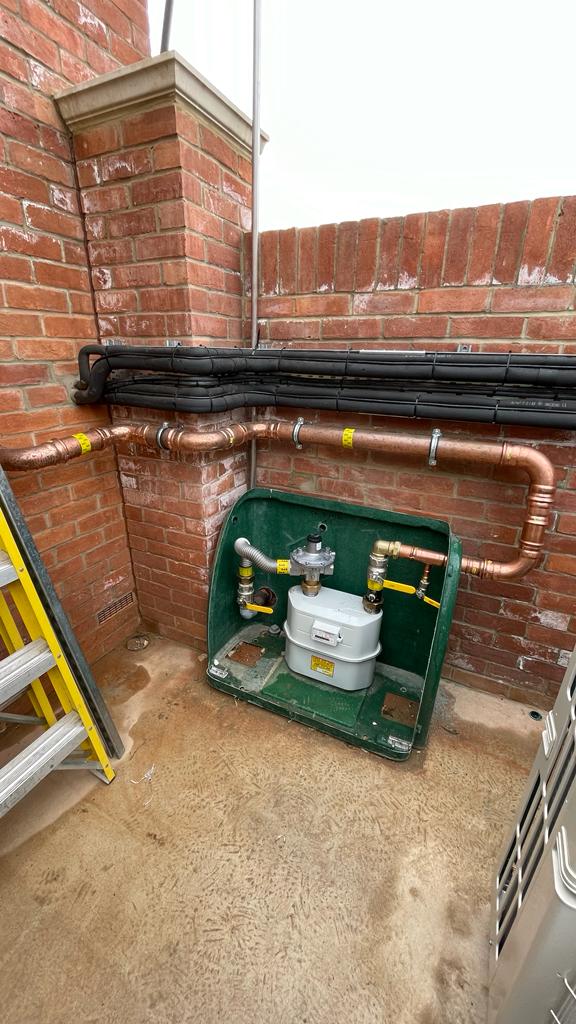 a box connected by pipes in front of a brick wall