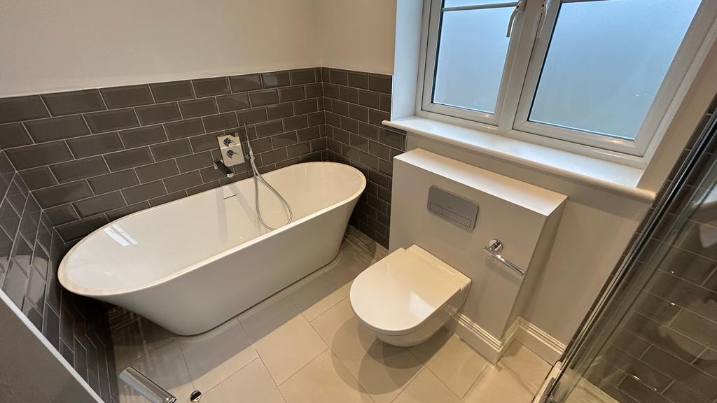 a tiled bathroom with a bath, toilet and window