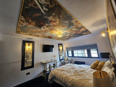 a bedroom with a large painting on the ceiling