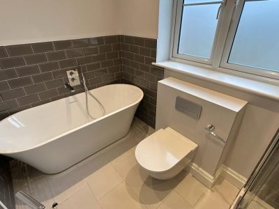 a tiled bathroom with a bath, toilet and window