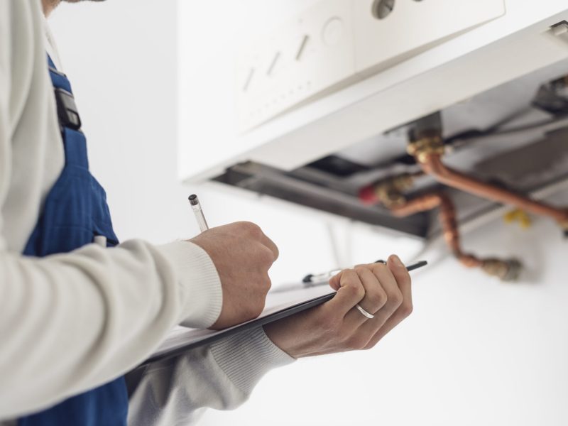 Professional plumber checking a boiler at home and writing on a clipboard